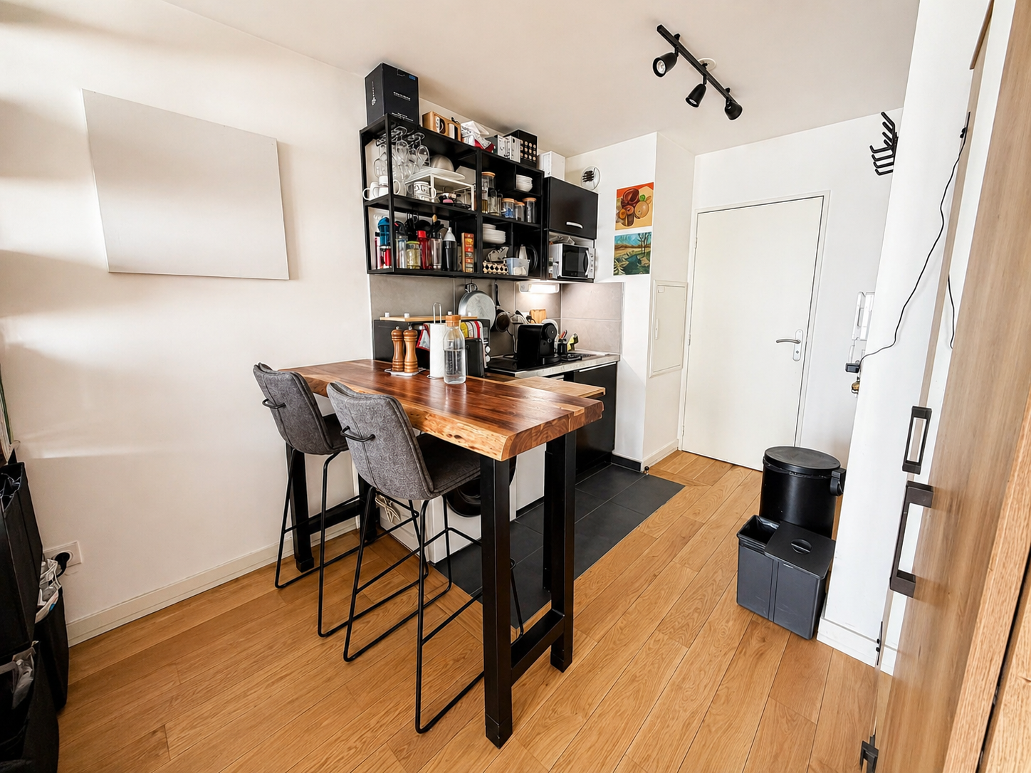 Coin repas : table haute en bois massif, tabourets et kitchenette équipée en fond
